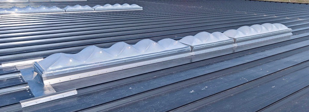 Sequenced standing seam metal roof skylights with multiple prismatic domes joined end to end on a continuous curb